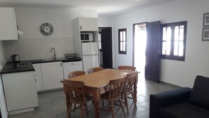 A compact living space with a wooden dining table, chairs, a sofa, a kitchen area with white cabinets, a microwave, and a refrigerator. - Country house with exclusive pool (Paderne)