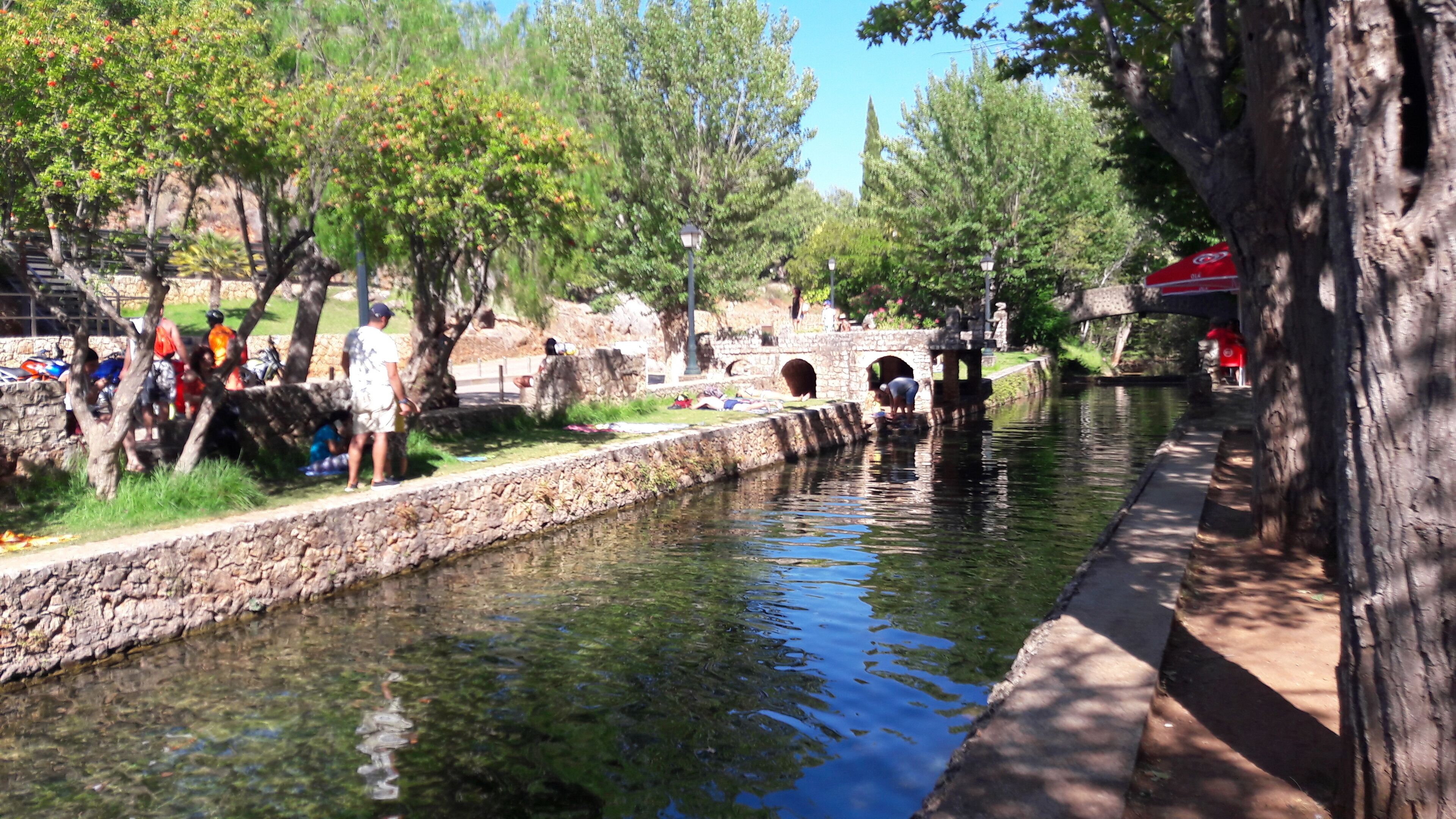 A canal with stone walls, trees, and people near the water.