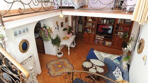 A multi-level interior with a staircase, a living area with a sofa and TV, and a bookshelf.