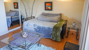 A bedroom with a bed, a glass coffee table, a mirror, and a bedside table.
