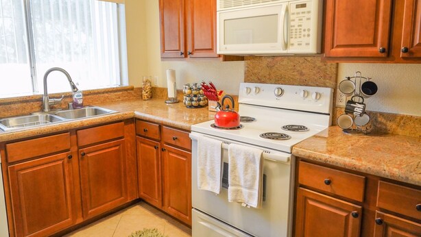 A kitchen with wooden cabinets, a white stove, a microwave, and a granite countertop.