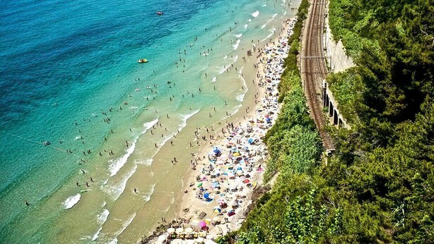 Una playa con una vía de tren que discurre paralela a la orilla, rodeada de abundante vegetación.