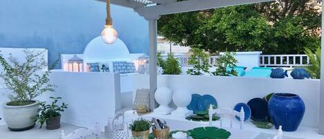 A rooftop terrace with a white table set for dining, surrounded by potted plants and decorative items.