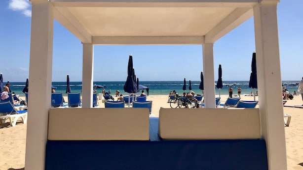 En strandpaviljong med utsikt över havet, blå solstolar och parasoller.