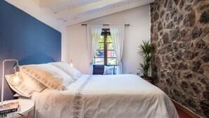 A bedroom with a bed, a nightstand, a lamp, a window with curtains, a potted plant, and a stone wall. - Canarian house with pool, barbecue, wifi, netflix (La Orotava)
