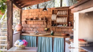 A rustic kitchen with brick walls, a wooden counter, and shelves holding dishes and pottery. - Canarian house with pool, barbecue, wifi, netflix (La Orotava)