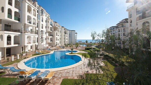 A resort with a central swimming pool, multiple balconies, and a view of the sea. - Marina de la Duquesa 225 (Manilva)