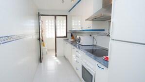 A narrow kitchen with white tiled walls, a built-in oven, and a microwave on the counter. - Marina de la Duquesa 225 (Manilva)