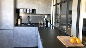 Une cuisine moderne avec des meubles gris, un évier noir et une planche à découper en bois sur laquelle sont posées des oranges.