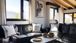 Un salon moderne avec un canapé en cuir noir, une table basse en marbre blanc et de grandes fenêtres offrant une vue sur les montagnes.