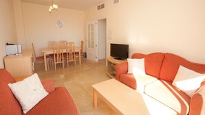 A living room with a sofa, a coffee table, a TV, a dining table with chairs, and a small cabinet.