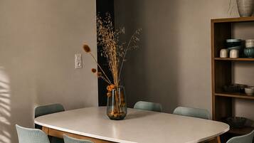 Un comedor moderno con una mesa redonda, seis sillas, un jarrón con plantas secas y una estantería con diversos objetos.