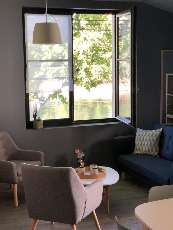 Un salon moderne avec une grande fenêtre, un canapé, un fauteuil et une petite table sur laquelle se trouve un plateau avec des tasses.