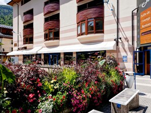 A hotel with a covered outdoor seating area, a sign for 'Salle de Loungue Restaurant', and a variety of plants and flowers. - Cozy studio 2 ppl, city center, WIFI, balcony, pets allowed (Brides-les-Bains)