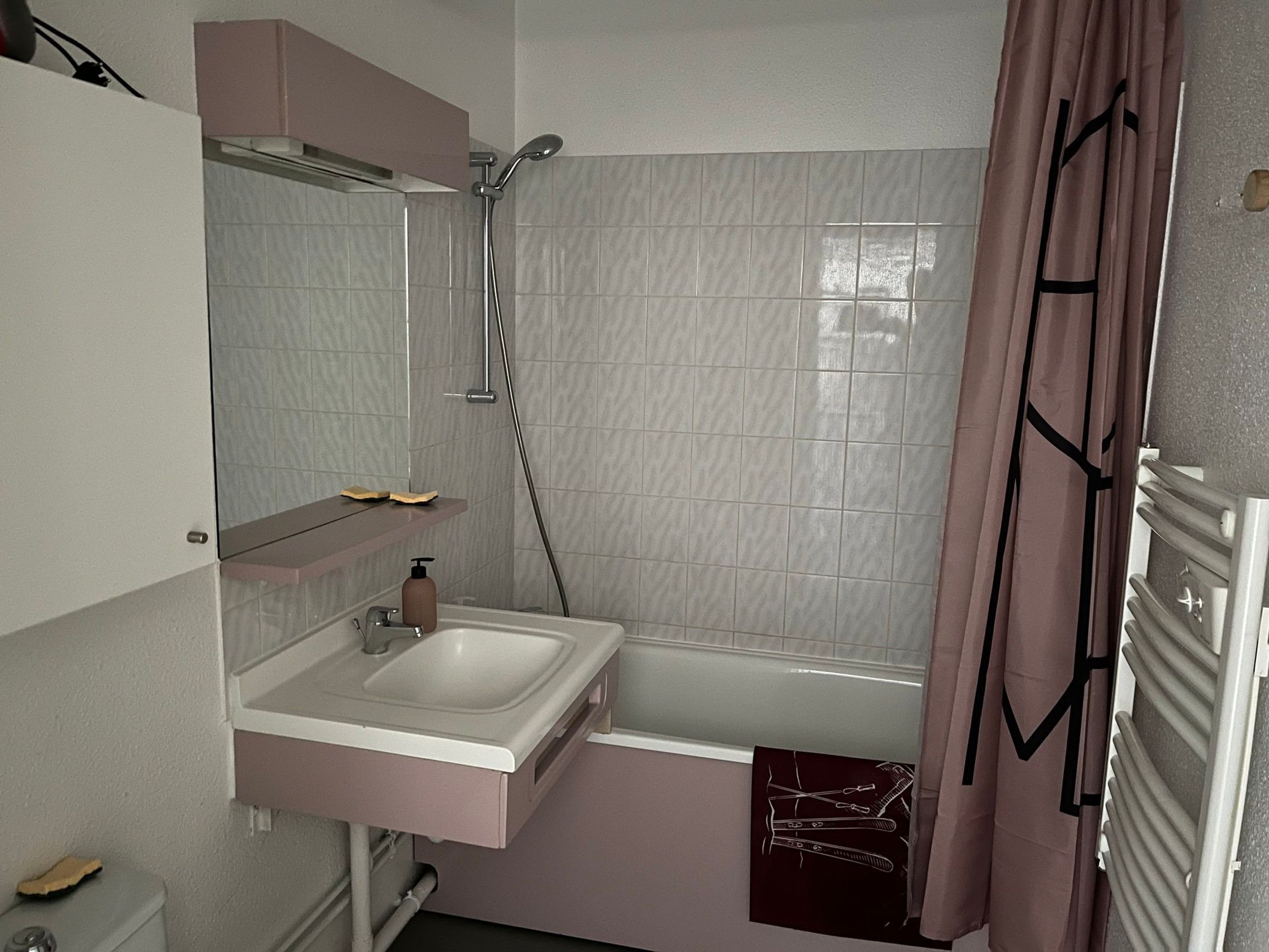 Et badeværelse med vask, spejl, brusebad og håndklædetørrestativ.