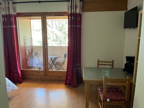 Una habitación con suelo de madera, una mesa de vidrio y una silla. Posee un ventanal corredero que da a un espacio exterior con una mesa y sillas.