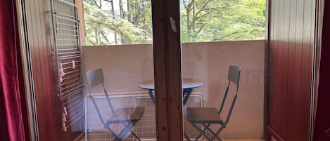 Un balcón con una mesa, dos sillas, un tendedero y vistas a una ladera boscosa.