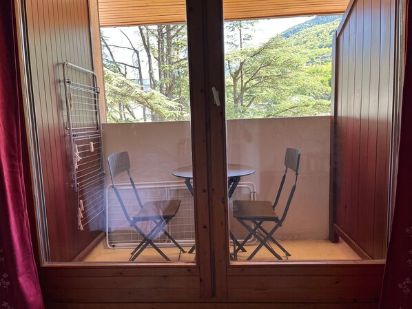 A balcony with a table and two chairs, a drying rack, and a view of a forested hillside.