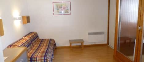 A small room with a bed, a wooden bench, a dresser, a radiator, and a sliding glass door.
