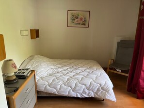 A neatly made bed with a white quilt, a bedside table with a lamp, a chair, and a wall-mounted picture.