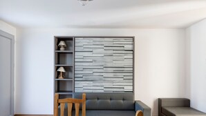 Een moderne woonkamer met een grijze bank, een houten eettafel en een wandplank met decoratieve spullen.