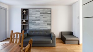 Een moderne woonkamer met een grijze bank, een houten eettafel en een inbouwkast met lampen.