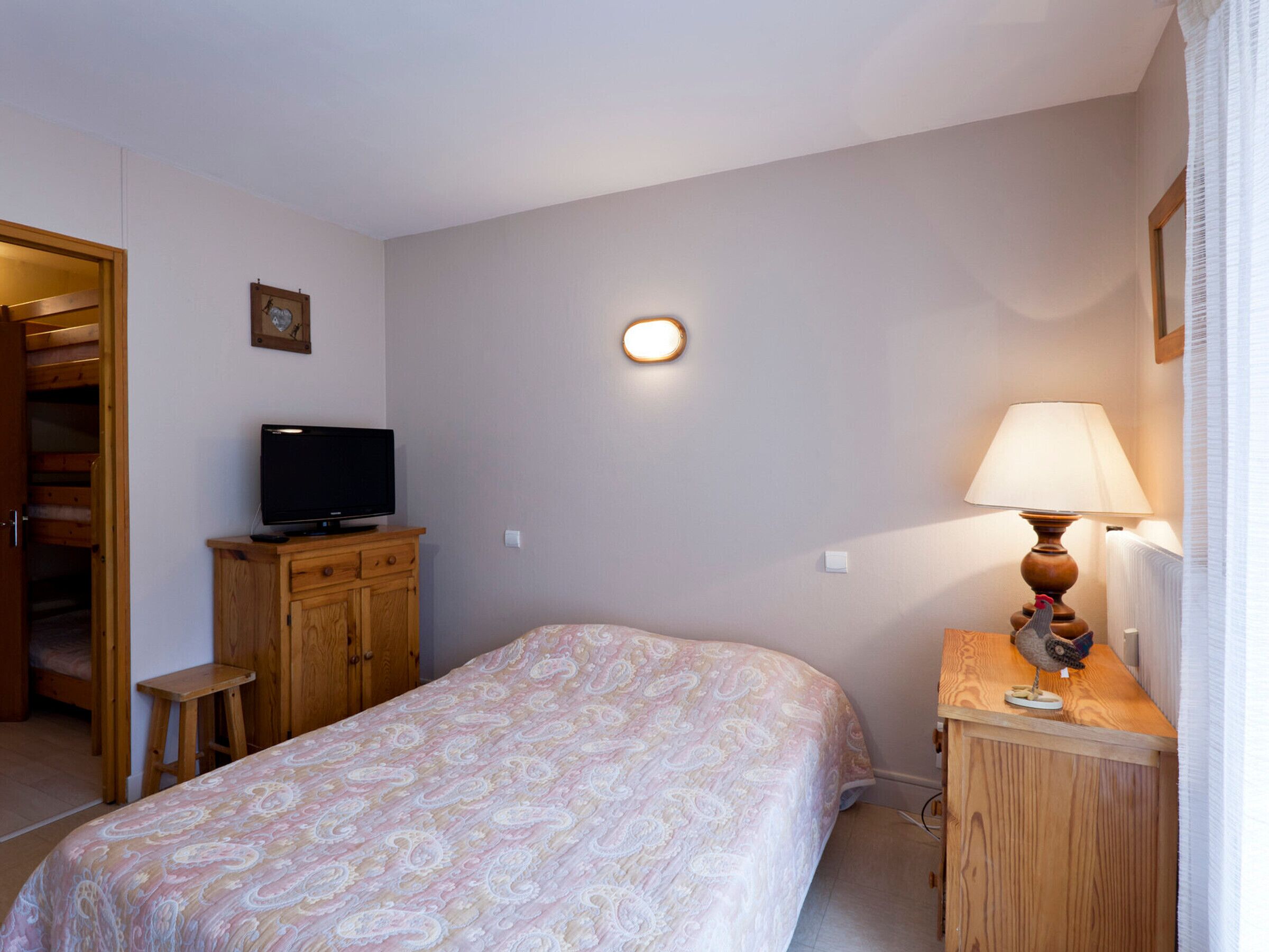 Een slaapkamer met een bed, een televisie op een houten kast, een bedlamp en een foto aan de muur.