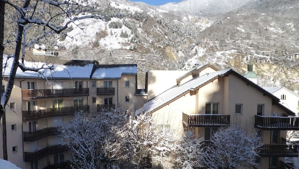 Un pueblo cubierto de nieve en la montaña, con edificios de varios pisos, balcones y un cielo despejado.