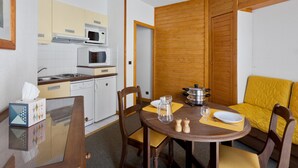 Una cocina compacta con microondas, estufa y pileta, una mesa de comedor con sillas y un sofá amarillo.