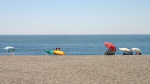 Une plage avec des gens assis sous des parasols, un ciel dégagé et la mer.
