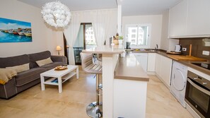 Un espacio habitable compacto con sofá, mesa de comedor, kitchenette y vistas al exterior.