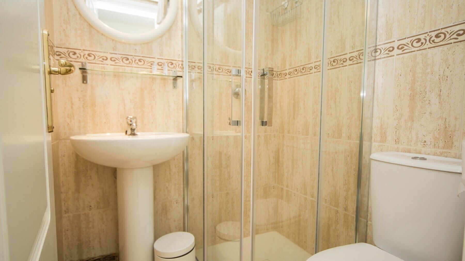 Et badeværelse med et glasafskærmet brusebad, en pedalvask og et toilet.