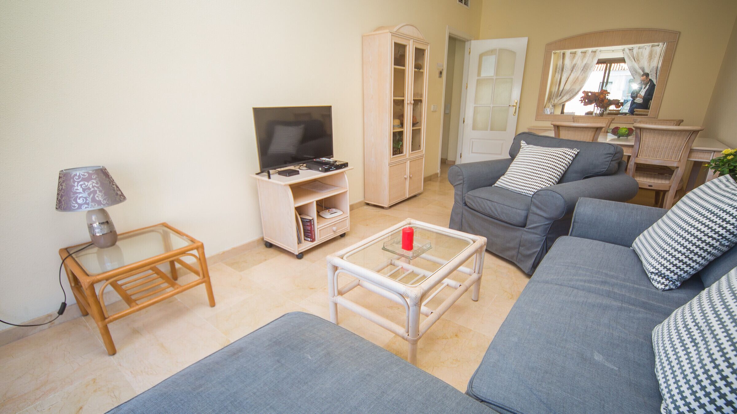 Una sala de estar con un sofá, una mesa de centro de vidrio, un televisor, un mueble y una lámpara.