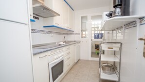 A compact kitchen with white cabinets, a built-in oven, and a stainless steel range hood. - Marina de la Duquesa 722 (Manilva)