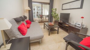 A modern hotel room with a bed, a TV, a desk, and a balcony with a view of buildings. - Marina de la Duquesa 722 (Manilva)