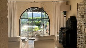 A room with two beds, a table, and a view of a garden through a large arched window. - Prestigious estate in Ménerbes. large heated swimming pool. large landscaped grounds. (Ménerbes)