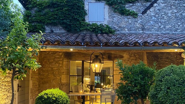 A stone building with a tiled roof, a wooden door, and a patio area with a table and chairs. - Prestigious estate in Ménerbes. large heated swimming pool. large landscaped grounds. (Ménerbes)