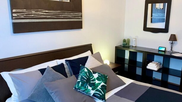 Habitación de hotel con cama, almohadas, mesita de noche, espejo y escritorio con lámpara.