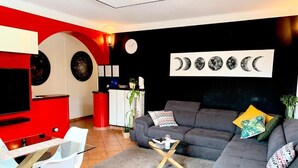 Una sala moderna con un sofá gris, detalles en rojo, un televisor de pantalla plana y un reloj de pared.