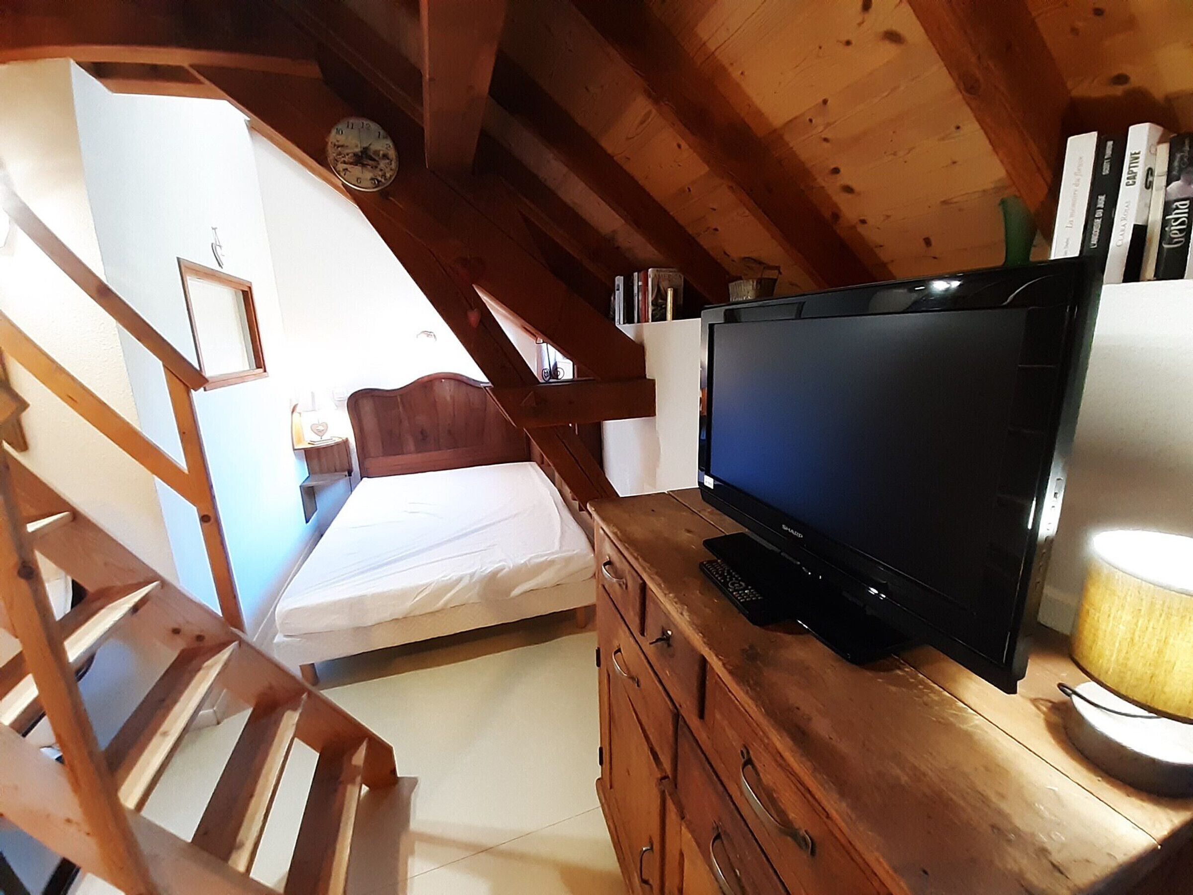 Un dormitori amb un llit, un prestatge de fusta, un televisor i un rellotge a la paret.