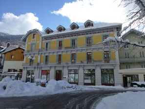 A multi-story building with balconies, a ground floor shop, and snow-covered surroundings.