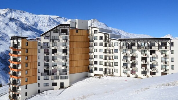 Un hotel moderno de varios pisos con fachada de madera, situado en una zona montañosa nevada con cielos azules despejados.