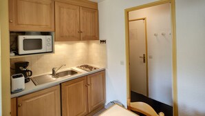 Cocina compacta con armarios de madera, un microondas, un lavamanos y una encimera.