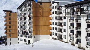 Un hotel moderno de varios pisos con fachada de madera y balcones, con el paisaje de una montaña nevada al fondo.