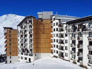 Un moderno hotel a più piani con facciata in legno e balconi, con vista su montagne innevate.