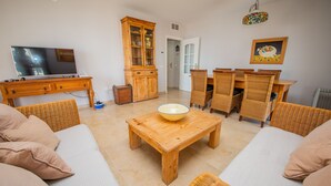 A living room with a wooden coffee table, wicker furniture, a television, and a cabinet.