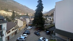 Vista de la calle con coches aparcados, edificios y una montaña al fondo.