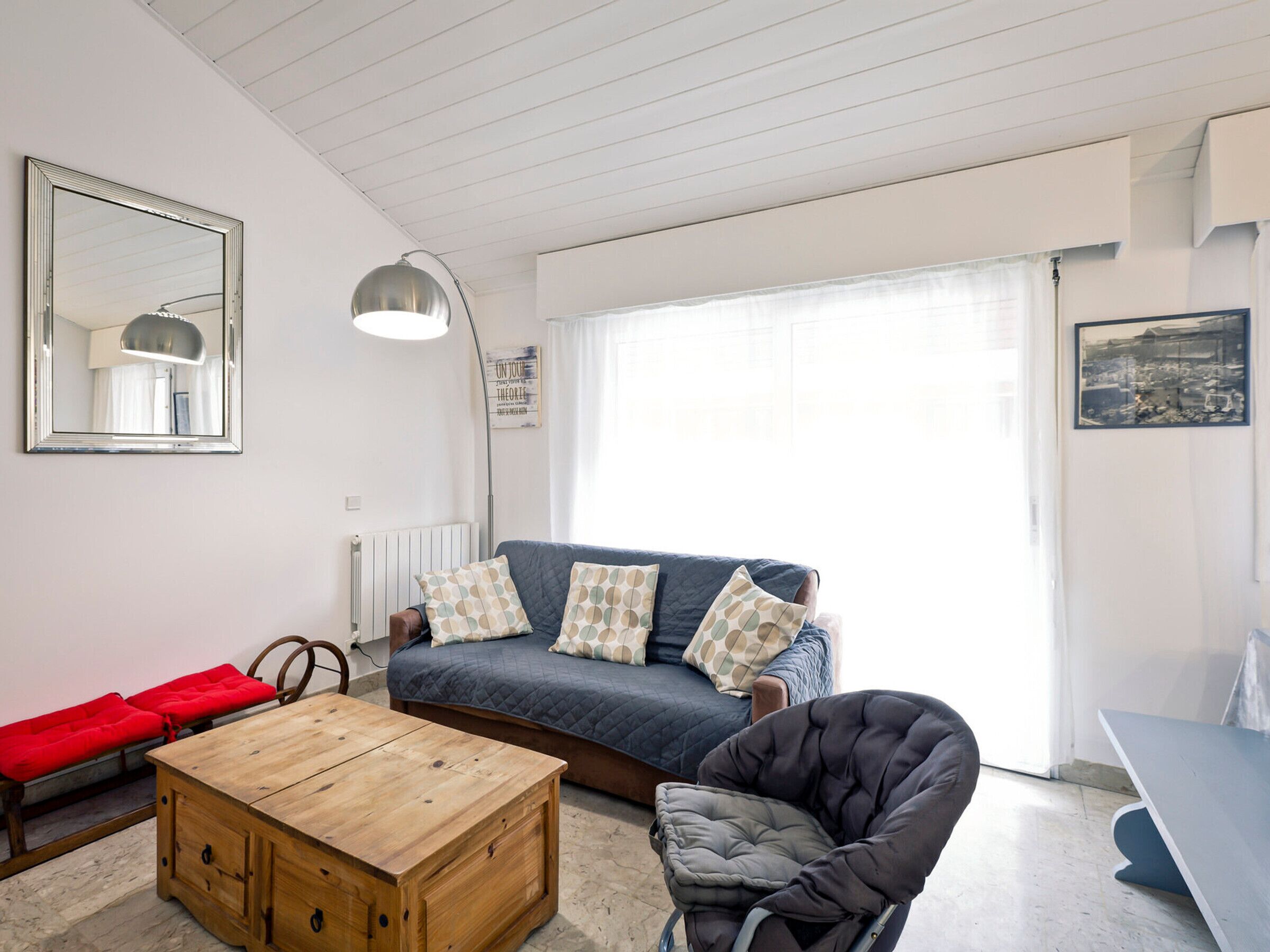 Una sala de estar acogedora con un sofá, una mesa de centro de madera, una silla y un gran ventanal con cortinas.