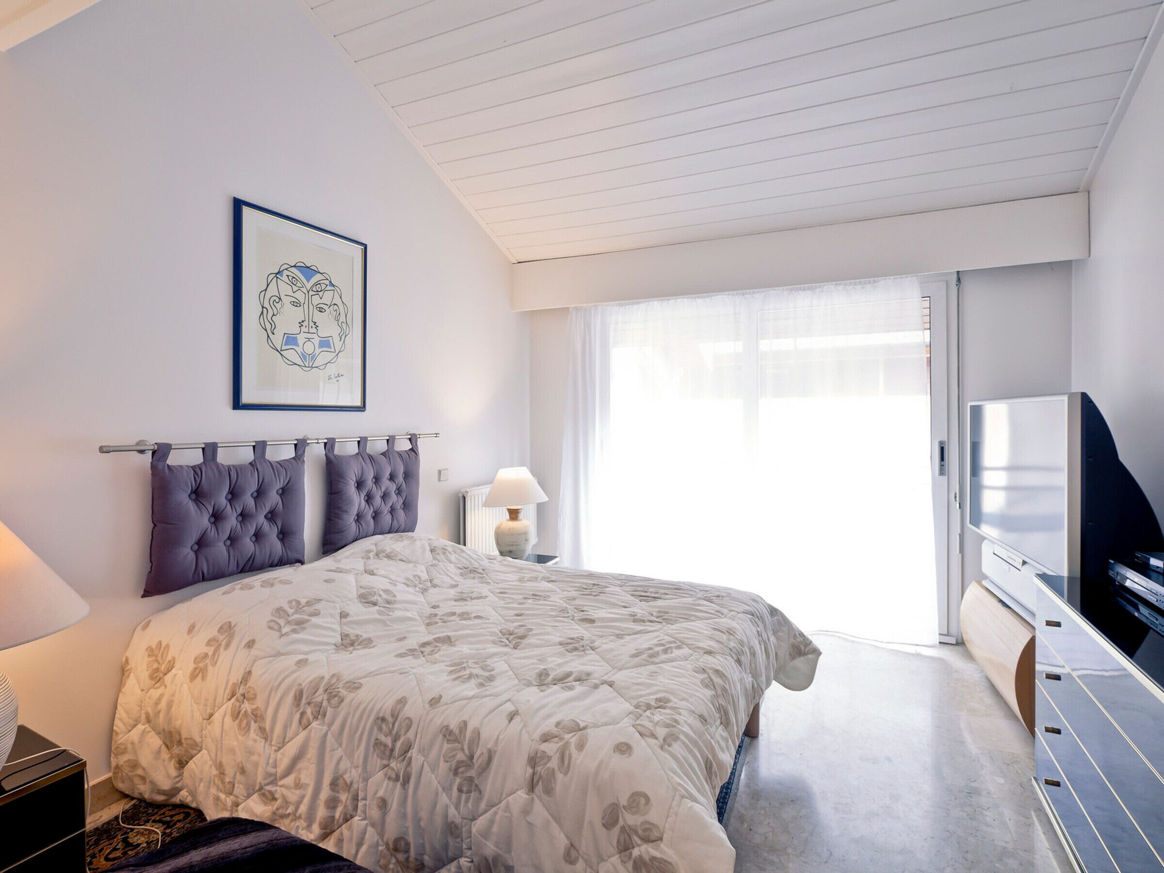 A modern bedroom with a large bed, a television, and a framed artwork on the wall.