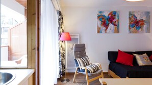 Un salon moderne avec un plancher en bois, un canapé noir agrémenté de coussins rouges et à rayures, un fauteuil à rayures et deux tableaux abstraits aux couleurs vives accrochés au mur.